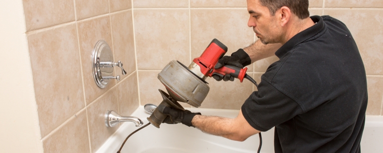 A plumber with plumbing insurance unclogging a shower drain