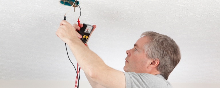 An insured Electrician using meter to test ceiling outlet

