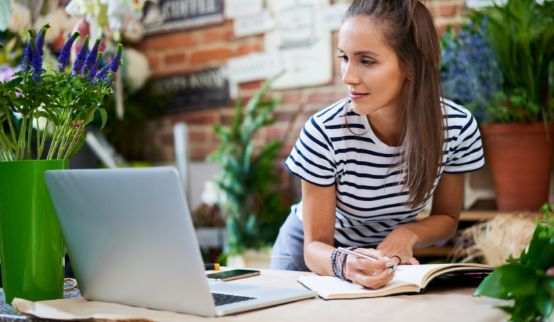 A woman makes notes while looking at her laptop.