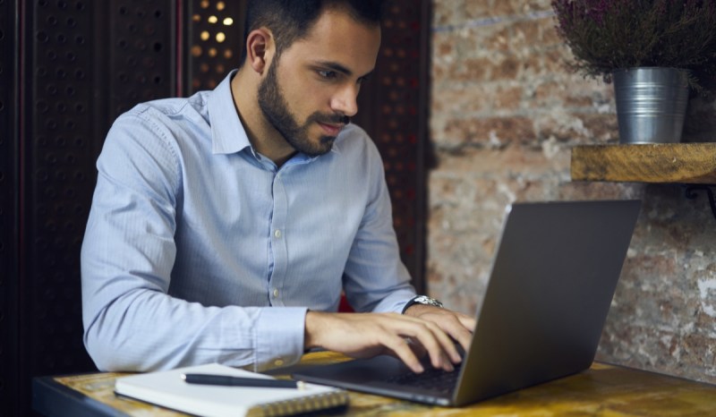 Man in light blue button down shirt typing on a laptop.