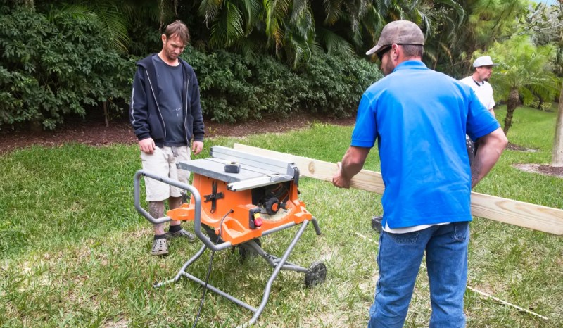 Two men working outside while securing a wooden board to a worktable.