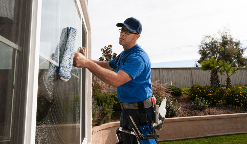 A man who has learned how to start a window cleaning business is using a squeegee to clean a customer’s window