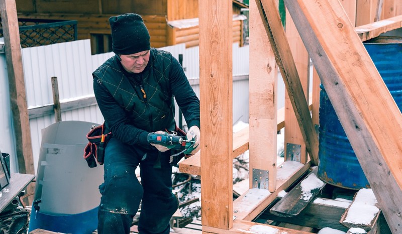 Contractor wearing black using drill on wooden frame