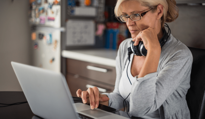 A woman with headphones around her neck works at her laptop.