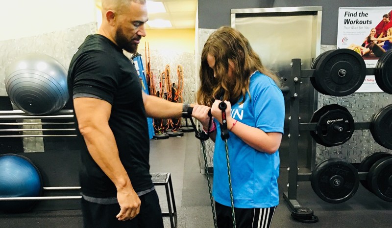 A male personal trainer is showing his female client how to use gym equipment