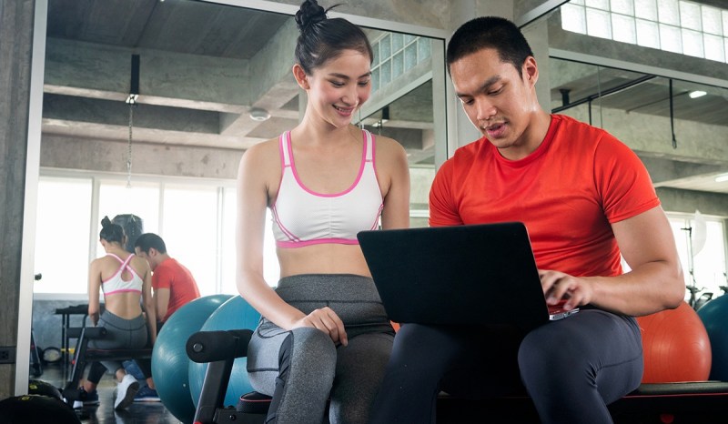A personal trainer is using his laptop to share information with a female client