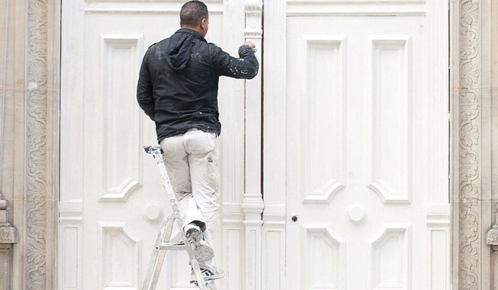 A contractor with painters’ insurance is painting a client’s door