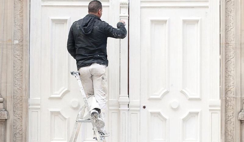 A contractor with painters’ insurance is painting a client’s door