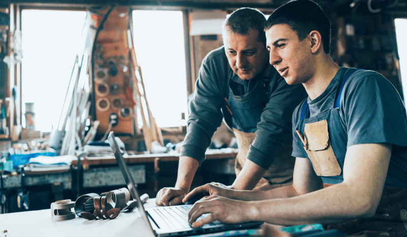 Two men in a workshop looking at a laptop screen.