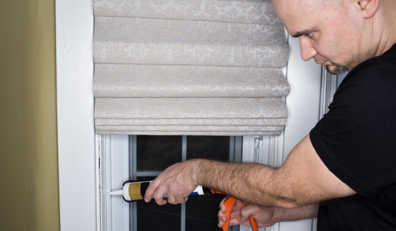 Contractor sealing a window using a caulking gun.