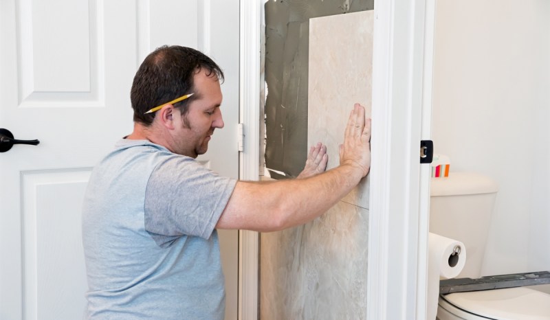 Contractor installing new tile to bathroom wall.